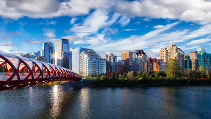 Fototapeta premium Peace Bridge across Bow River during a vibrant summer sunrise. Urban Downtown City Skyline. Taken in Calgary, Alberta, Canada.
