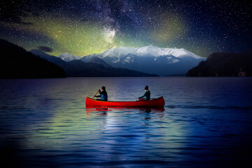 Adventurous People on a Red Canoe in a Lake. Night Sky with Stars and Northern Lights. Dream Mood. Landscape taken in Harrison Hotsprings, British Columbia, Canada.