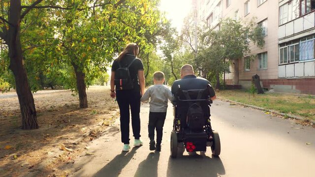 wheelchair man. Handicapped man. young disabled man in an automated wheelchair walks with his family, wife and small child, along city alley on sunny autumn day. back view