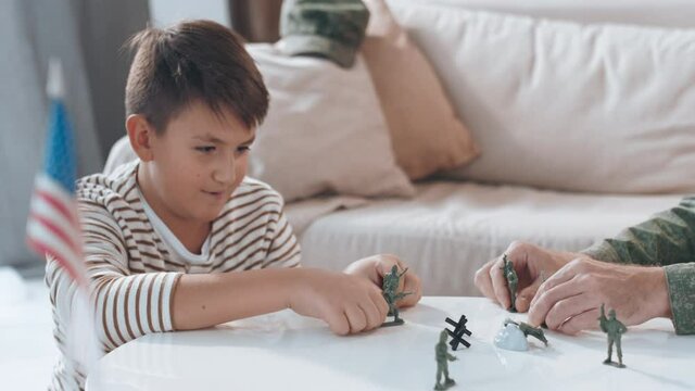 Handheld shot of boy and his unrecognizable father in military uniform playing with toy soldiers in living room