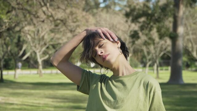 Parallax shot of a caucasian woman slowly stretching her neck at park . High quality 4k footage