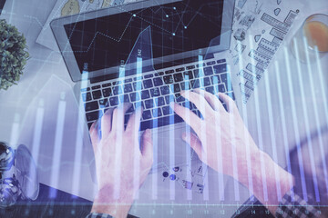 Plakat Double exposure of man's hands typing over laptop keyboard and forex chart hologram drawing. Top view. Financial markets concept.