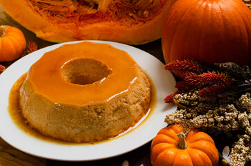 Flan de calabaza. Postre elaborado con calabaza,  servido en plato blanco, sobre mesa de madera decorado con tema otoñal.