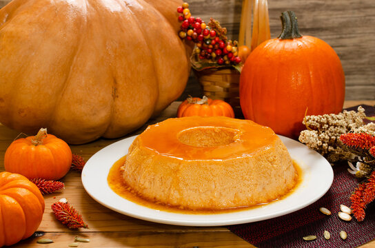 Flan de calabaza. Postre elaborado con calabaza,  servido en plato blanco, sobre mesa de madera decorado con tema oto&ntilde;al.