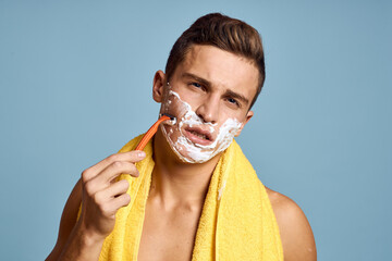Man with razor on blue background and white foam yellow towel cropped view