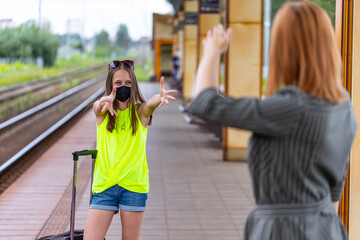 Fototapeta premium Safe family travel. Hugs of mother and daughter when meeting. Protection of face with masks after pandemic. Railway station.