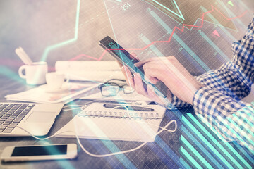 Double exposure of man's hands holding and using a digital device and forex graph drawing. Financial market concept.