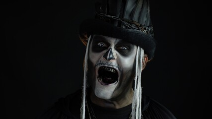 Sinister man with Halloween skeleton makeup turning his head and looking at camera, trying to scare