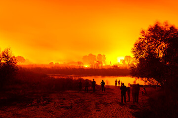 People near the river look at burning fields and forest