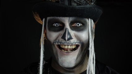 Close-up shot of creepy man in skeleton Halloween makeup opening eyes and looking spooky at camera