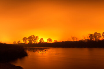 Fototapeta na wymiar Peaceful river against the background of a fiery sky of forest fires