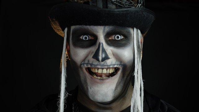 Close-up shot of creepy man in skeleton Halloween makeup opening eyes and looking spooky at camera