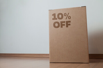 Cardboard box with 10% off order written on the box placed on the floor in an empty room with a neutral background. delivery concept. economy concept. business concept. shopping concept. copy space.