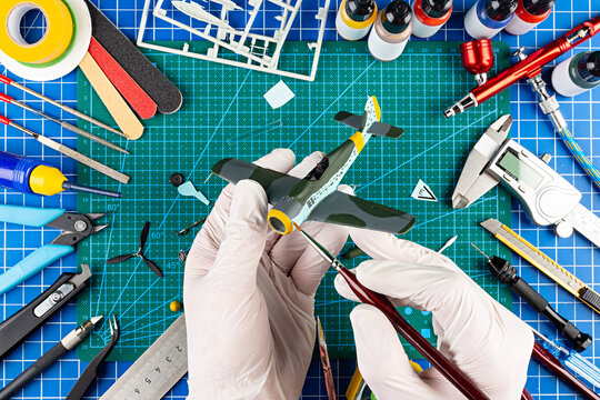 desktop view from above of assembly and painting of retro scale model fighter plane concept background. modeling tools airbrush gun paint kit parts blue green cutting mat knife and brush work desk