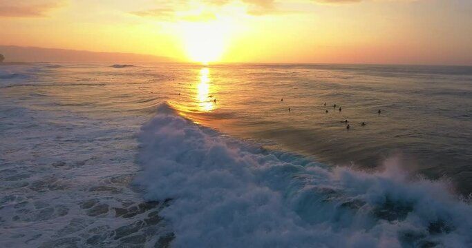 Surfers wait for waves at sunset in Hawaii, wide aerial