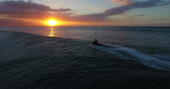 Wide aerial, person drives jet ski in Hawaii at sunset
