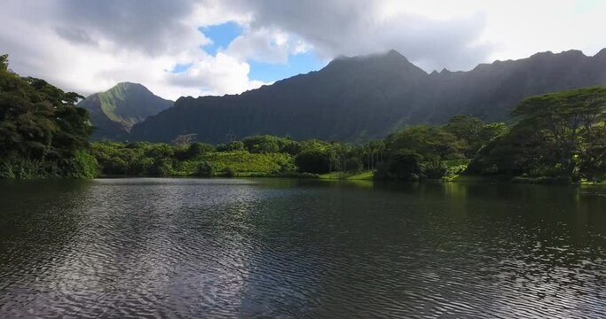 Wide aerial, river flows near mountains in Hawaii