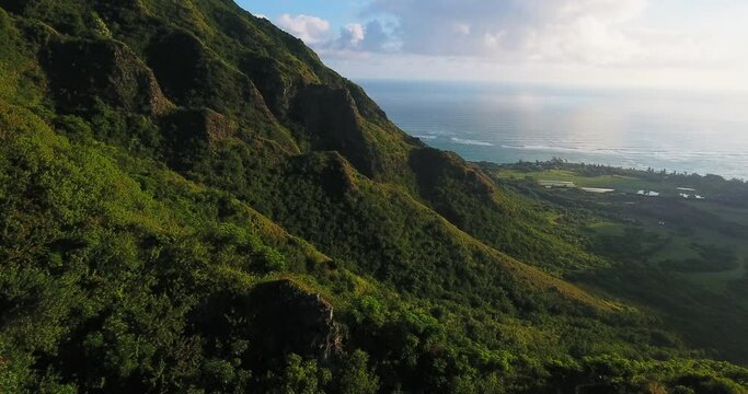 Sun shines over coastal Hawaiian mountains, wide aerial
