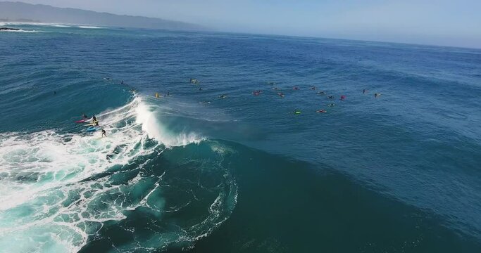 Surfers catch wave off Hawaiian coast, panning aerial