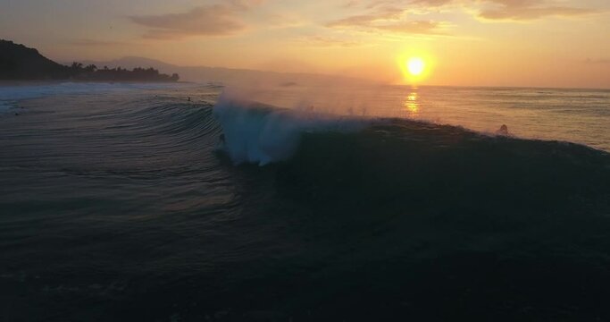 Wide aerial, wave crashes over surfer at sunset in Hawaii
