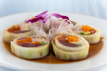 Assorted raw fish arranged in suhshi roll encased with cucumber delicately presented on a plate to eat.
