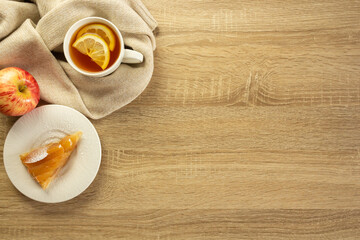 Sweater, cup of tea and apple pie on the wooden background with copy space. Cozy autumn or winter consept