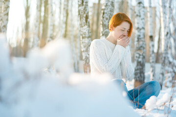Cute girl warms her hands with breath. Beautiful young woman froze in winter park, copy space.