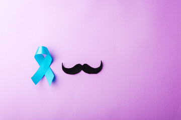 Black mustache paper and light blue ribbon, studio shot isolated on purple background, Prostate cancer awareness month, Fathers day, minimal November moustache concept