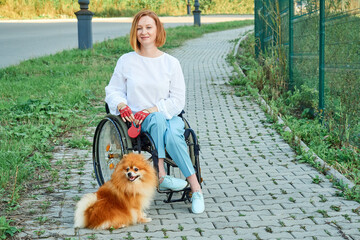A woman in a wheelchair walks with her dog outdoor.