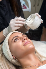 Applying a mask to the face in a beauty salon. Cosmetologist and procedure for rejuvenation and moisturizing.