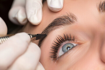Permanent eyebrow makeup. Cosmetologist applying tattooing of eyebrows. Close up shoot - obrazy, fototapety, plakaty