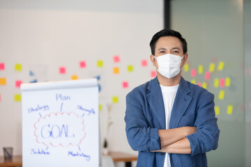 Fototapeta na wymiar Asian senior business man in casual wearing mask Standing cross arms in modern office or co-working space Due Covid-19 Flu Pandemic,Health care and Business Startup Concept