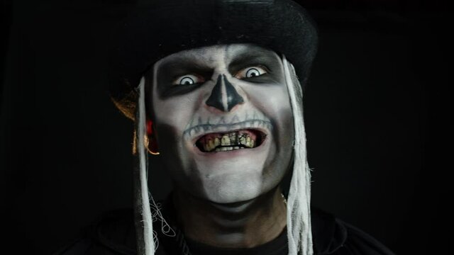 Sinister man with skull makeup appearing on black background, making faces and ominous smile