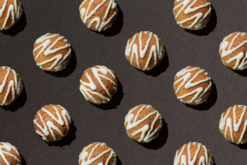 Pattern of delicious cookies with white glazed decoration on dark brown background with hard shadow. Creative minimal background.