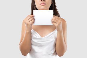 A Woman in white satin dress holding a white blank paper against a light gray background.
