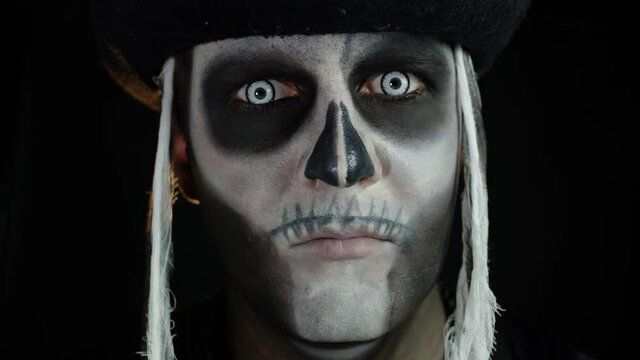 Scary man with carnival makeup of Halloween skeleton opening his eyes against black background