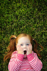 Surprised Little Red Haired Girl Lying in Grass Outside, Room for Text