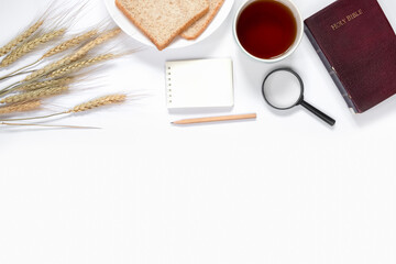Top view of breads, notebook, coffee, magnifying glass, and Holy Bible on white background