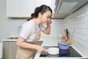 Young woman cooking in her kitchen standing near stove. Healthy lifestyle.