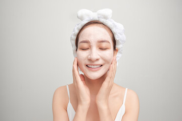 Cheerful young Asian woman with facial clay mask isolated on white background.