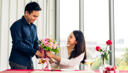 Young handsome man giving red rose surprise to girlfriend and holding red rose in valentine day at home