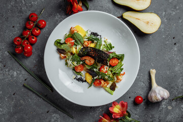 Traditional shrimp and mango salad in a restaurant. Fried shrimp salad with rosemary, mango, cherry tomatoes, salad mix, mango chili sauce.