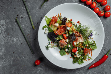 salad with ham and pear on dark gray background. jamon salad, salad mix, spinach, pear, cherry tomatoes, Dor Blue, capers and vinegar dressing Bianco
