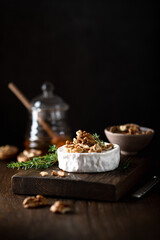 brie cheese with walnuts on a wooden cutting board . Selective focus, dark background