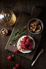 brie or camembert cheese with raspberries, honey and walnuts . Selective focus, dark background, top view