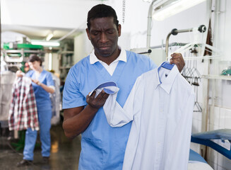 Experienced African-American man owner of laundry inspecting clothing after dry cleaning