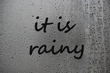 Inscription It is rainy written on wet window after rain