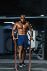 Fototapeta na wymiar Portrait of fit strong athletic man pulling rope in fitness club