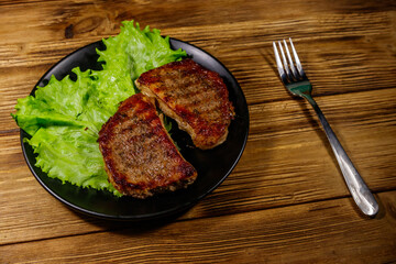 Grilled pork steaks with lettuce leaves on wooden table