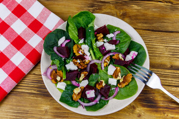 Tasty spinach salad with boiled beetroot, feta cheese, walnut and red onion on wooden table. Top view. Healthy vegetarian food